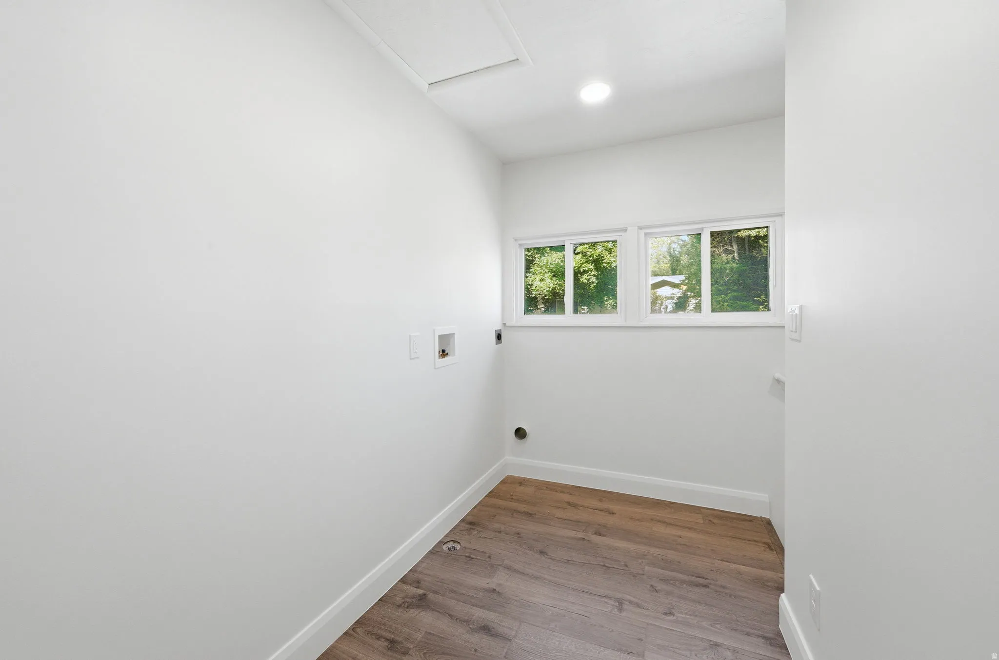 Utility room featuring wood-finish flooring, white walls, and three windows offering natural illumination