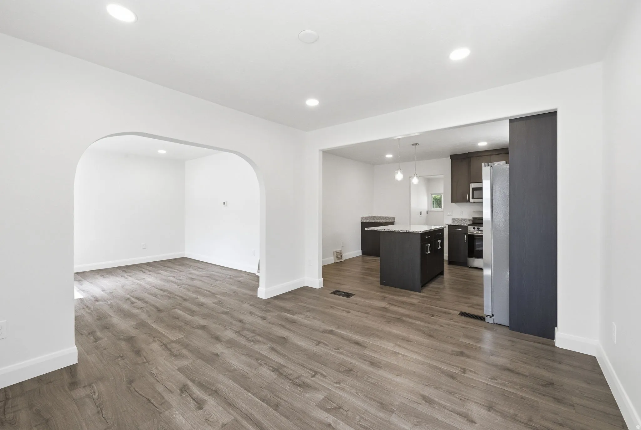 Spacious living area featuring wood-finish flooring, recessed lighting, and an arched entry