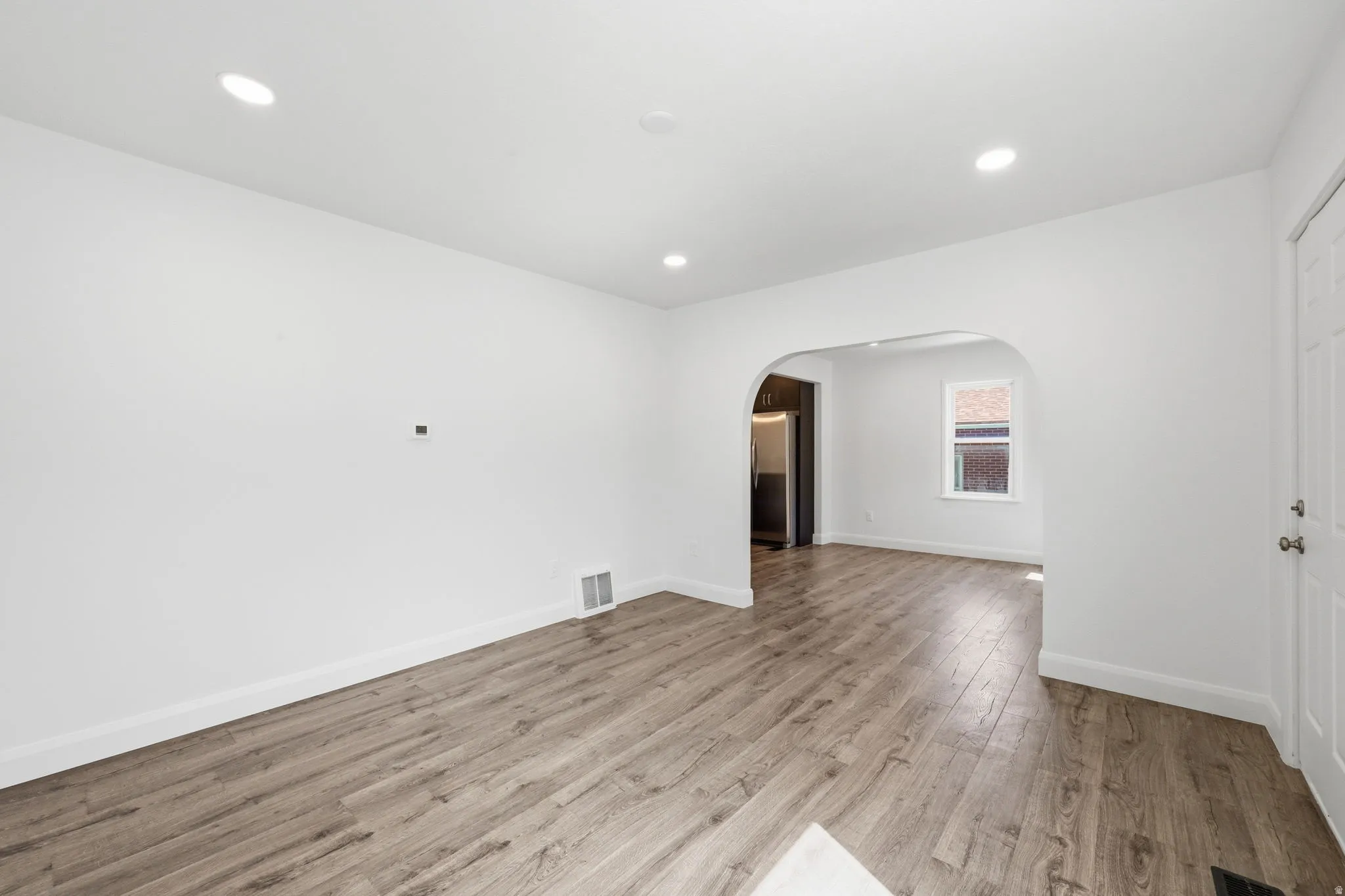 Open-concept living area featuring wood-finish flooring, recessed lighting, and a white paneled entry door