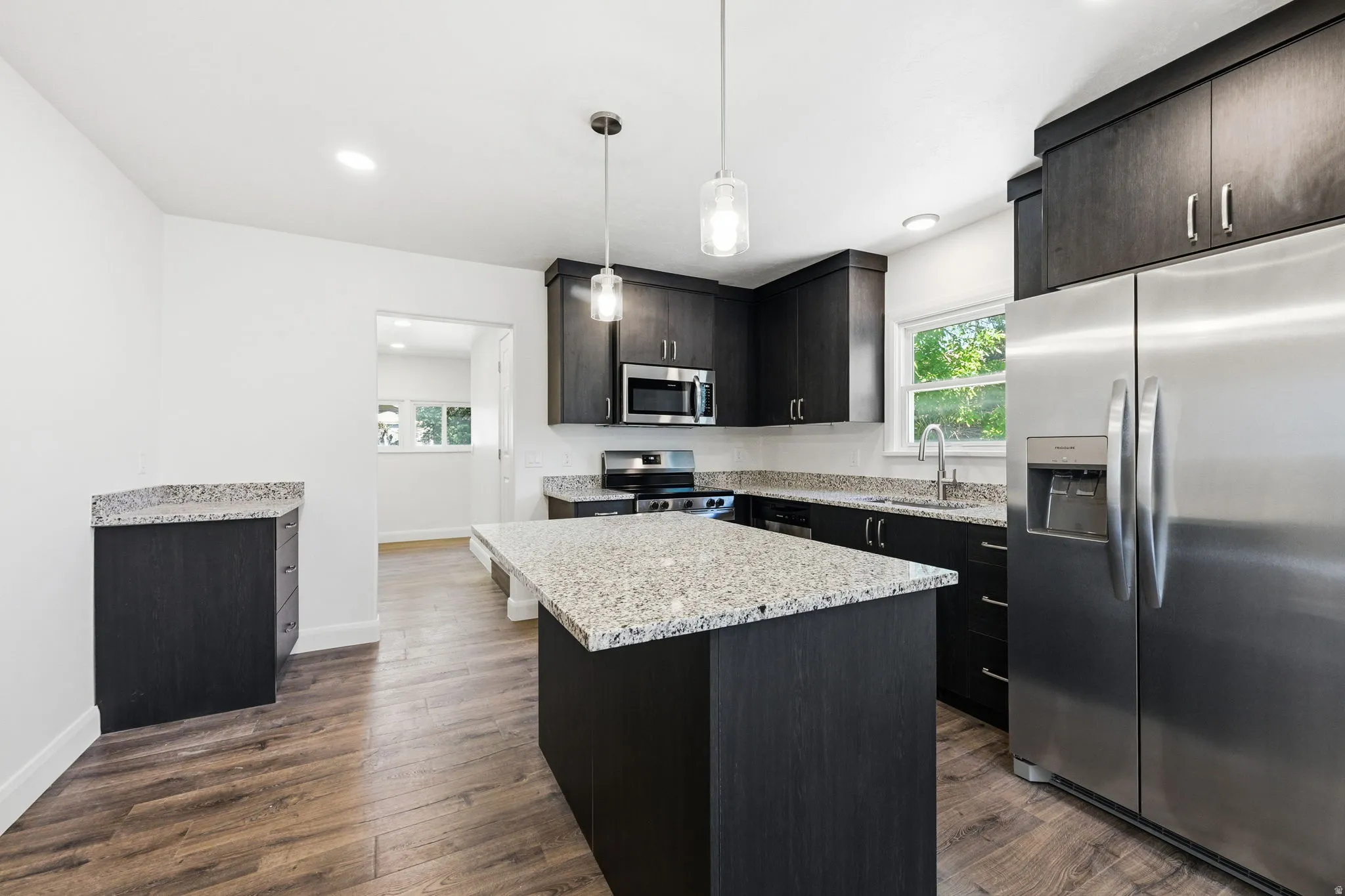 Spacious kitchen featuring dark wood-finish cabinetry, light speckled countertops, and stainless steel appliances