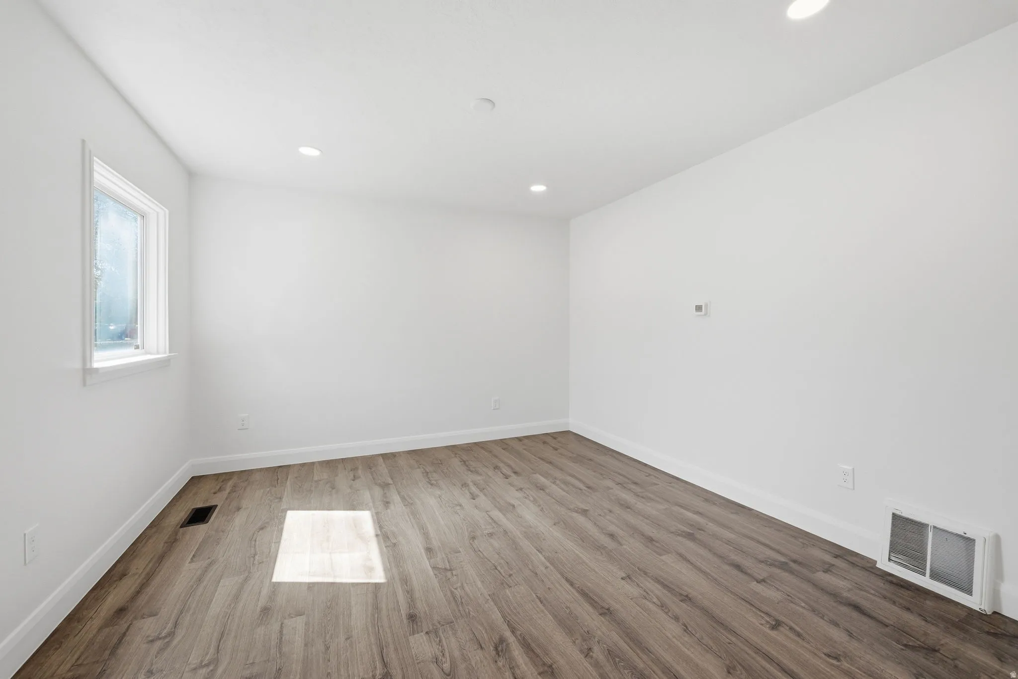 Spacious room featuring wood-finish flooring, recessed lighting, and a window with white trim