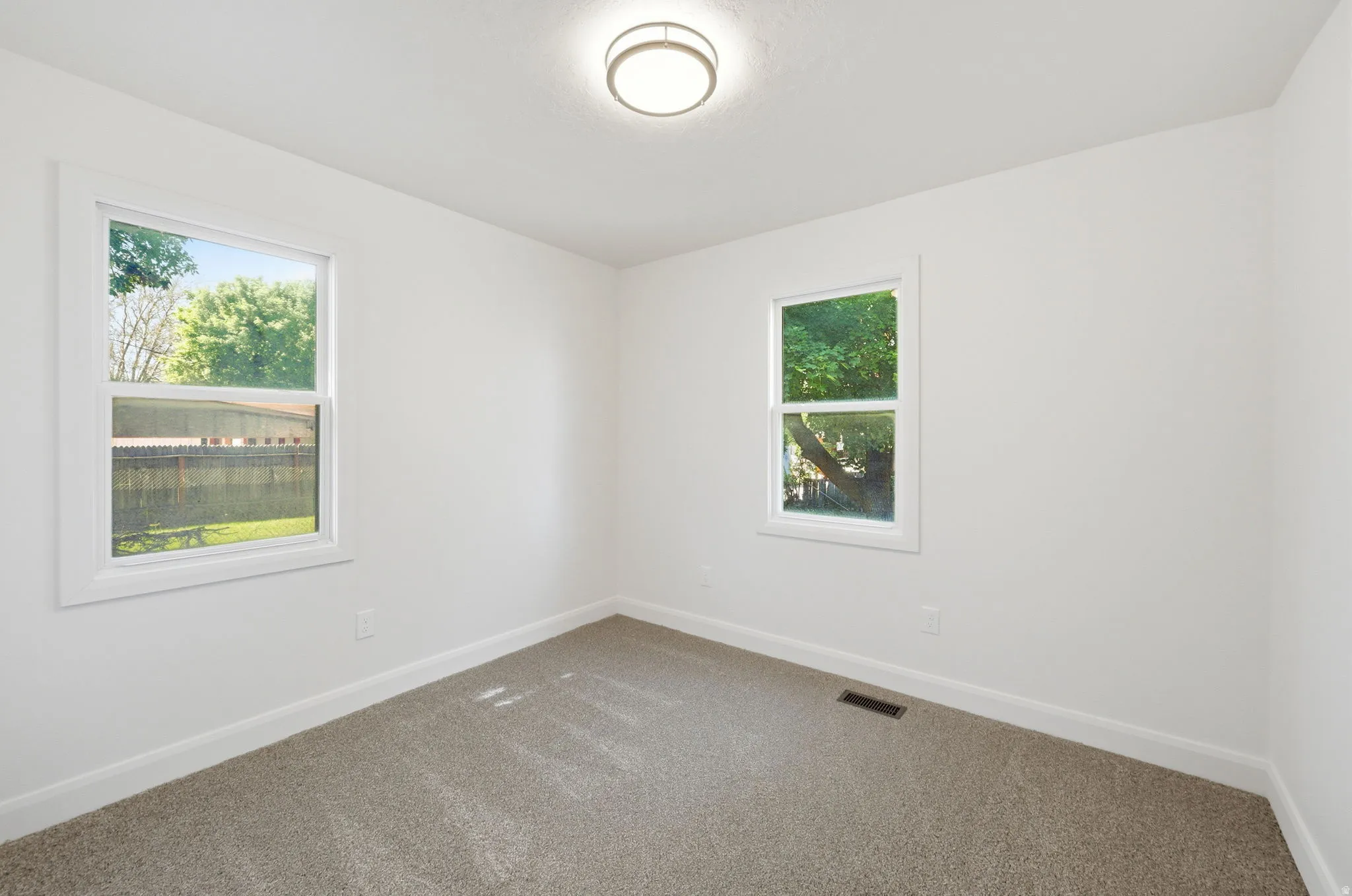 Bright room featuring two windows with white trim, neutral carpet flooring, and a flush mount ceiling light fixture