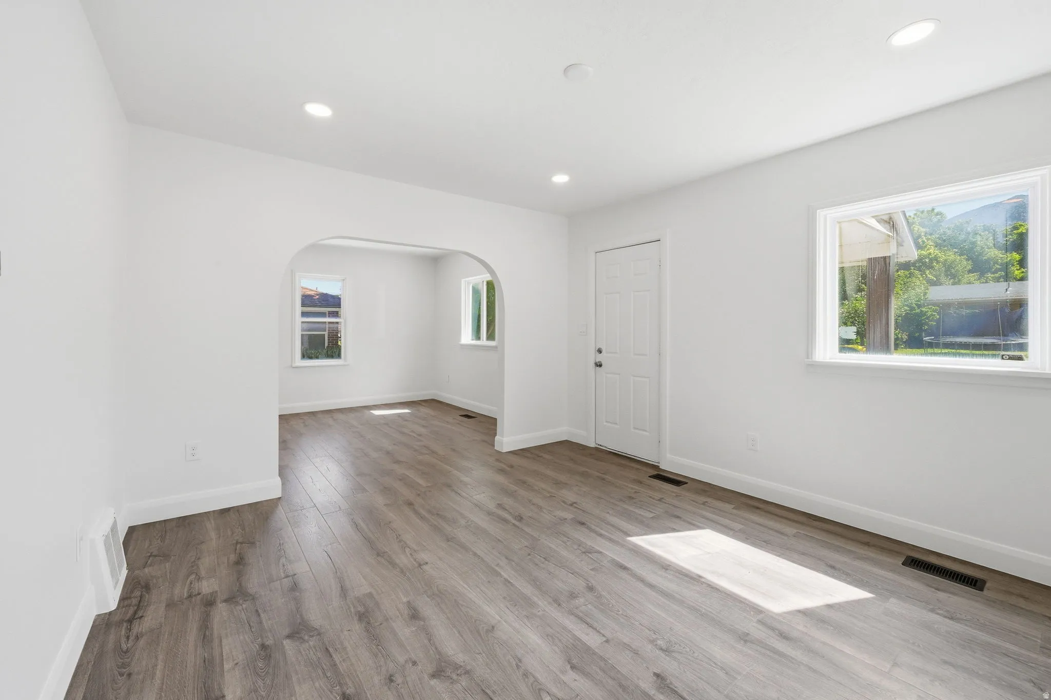 Open concept living area featuring wood-finish flooring, recessed lighting, white baseboards, and a white paneled entry door