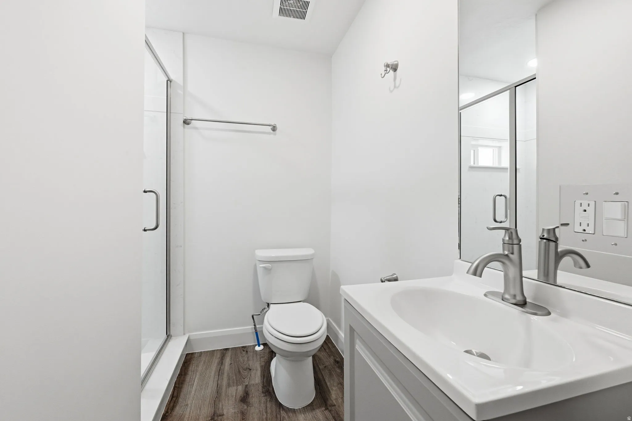 Bathroom featuring a glass-enclosed shower, wood-finish flooring, a white vanity with an integrated sink, a brushed nickel faucet, and a wall-mounted mirror