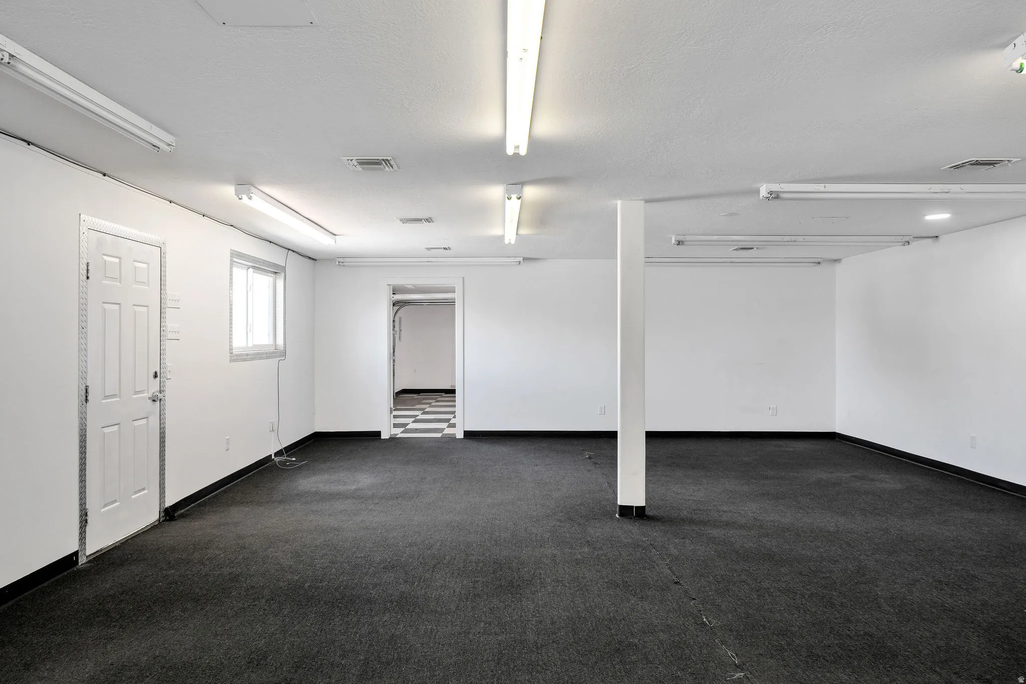 Spacious room featuring dark carpeting, white walls, and bright overhead fluorescent lighting