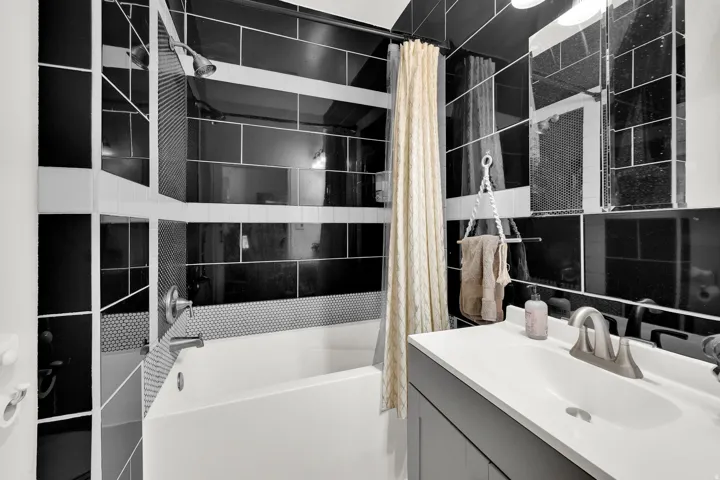 Full bathroom featuring a tub/shower combination with black subway tile and penny tile accents, a single vanity with a white countertop and basin, and a mirrored medicine cabinet
