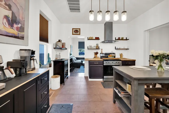 Spacious kitchen featuring stone flooring, dark wood-finish cabinetry, a stainless steel range with overhead vent hood, and an eat-at island
