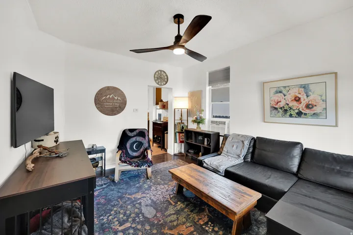 Living area featuring a ceiling fan with integrated lighting, white walls, and a window providing natural light