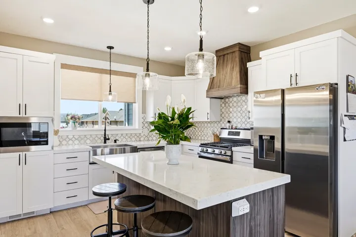 Kitchen featuring white shaker cabinetry, stainless steel appliances, a wood-finish range hood, and a central island with a light-toned countertop and dark wood-finish base