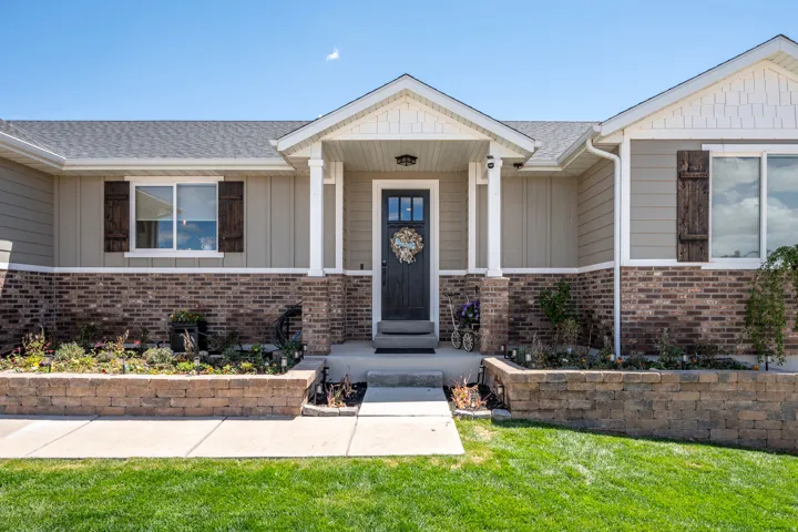 Front exterior featuring a covered entry, brick facade accents, board and batten siding, decorative window shutters, and a manicured lawn