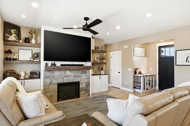 Living area featuring a stone-clad fireplace with wood mantle, built-in shelving, recessed lighting, and a ceiling fan