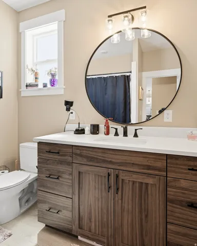 Bathroom featuring a wood-finish vanity with ample storage and matte black hardware, a round frameless mirror, and a contemporary four-light fixture