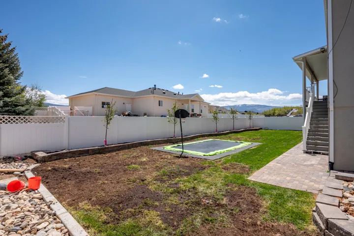 Expansive backyard featuring a partial grass lawn, a section of exposed soil, and a white privacy fence with lattice detailing
