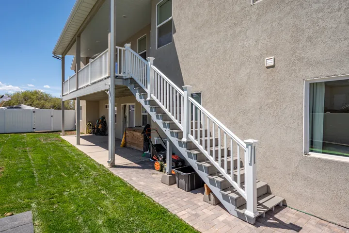 Exterior featuring a raised deck with white railing, a ground-level patio, and a stone paver pathway