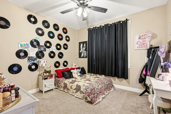 Carpeted bedroom with a ceiling fan, window with dark curtains, and light-colored walls