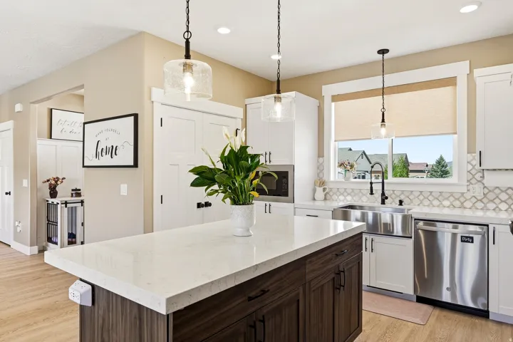 Kitchen featuring a spacious island with a light-toned countertop, white cabinetry with dark hardware, a stainless steel farm sink, and a decorative tile backsplash