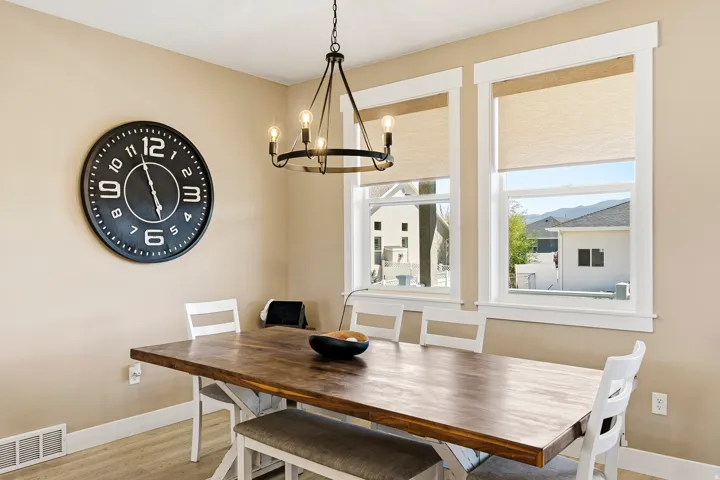 Dining area featuring a wood-finish table with white base, two large windows with roller shades, and a black metal chandelier