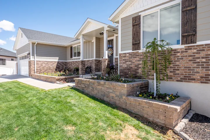 Exterior facade featuring a brick and siding combination, a covered porch entry, a two-car garage, and tiered stone retaining walls