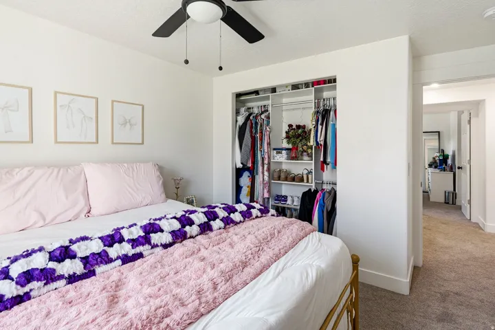 Bedroom featuring a built-in closet system with shelving and hanging rods, overhead ceiling fan with light, and light-colored walls