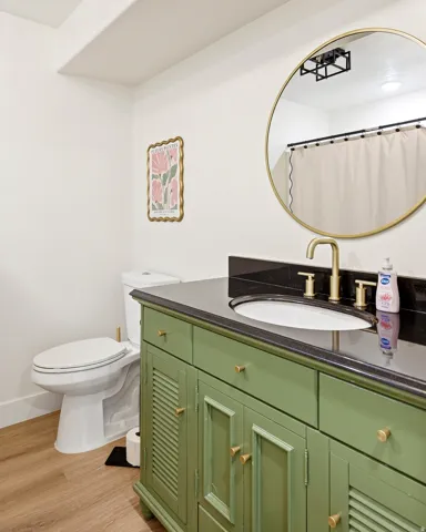 Bathroom featuring a green vanity with brass hardware, a black countertop, and an undermount sink