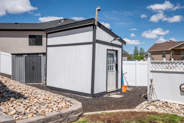 Freestanding white and black storage shed with a paneled door, accompanied by a smaller gray storage unit