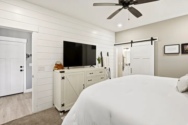 Bedroom featuring a shiplap accent wall, dark-toned ceiling fan, and a barn door leading to an adjacent space