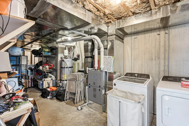 Basement utility space featuring a washer and dryer, water heater, water softener, and a furnace with exposed ductwork