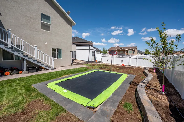 Spacious backyard featuring an in-ground trampoline, a manicured lawn, and a stone retaining wall
