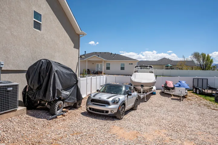 Expansive gravel parking area featuring a white vinyl fence and stucco exterior