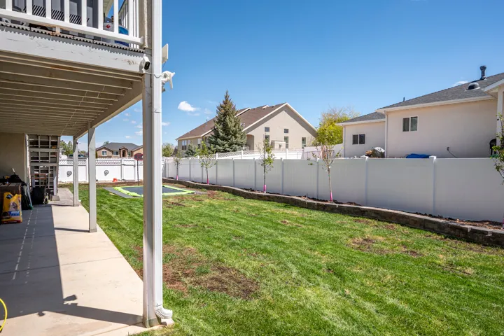 Expansive backyard featuring a manicured lawn, a full-height privacy fence, and a concrete patio beneath an upper-level deck