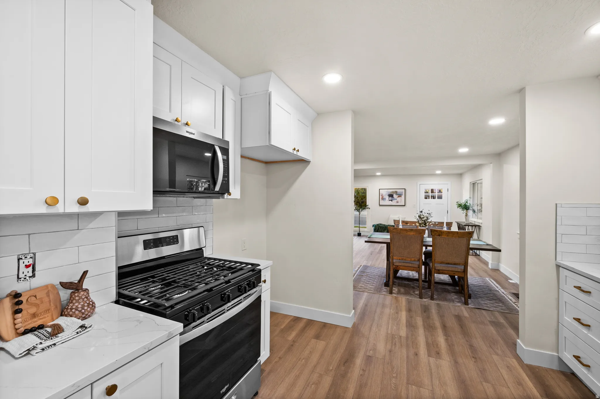 Kitchen featuring white shaker cabinetry, stainless steel range and microwave, light subway tile backsplash, and wood-finish flooring