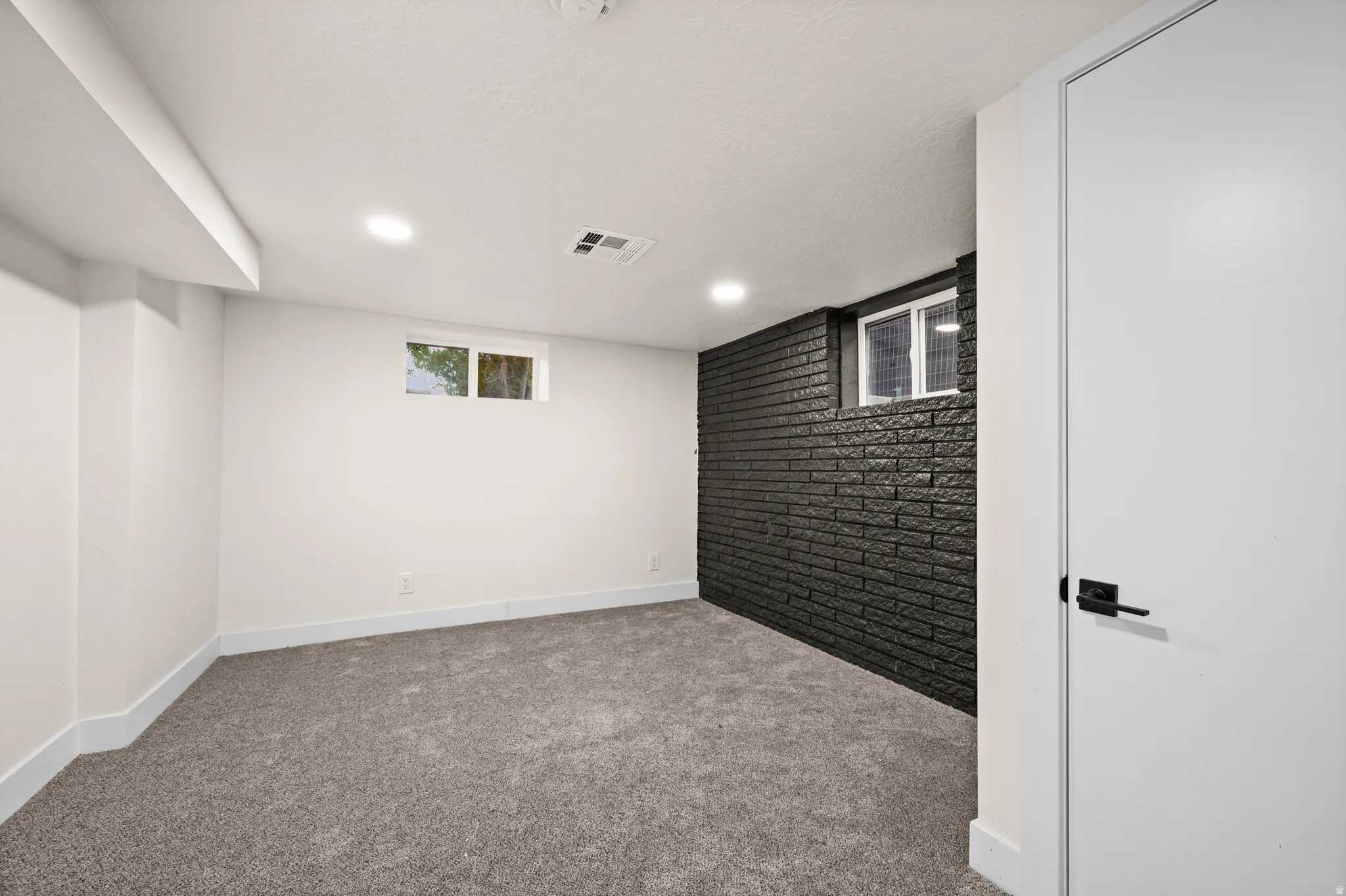 Room featuring a black painted brick accent wall, recessed lighting, and grey carpet flooring