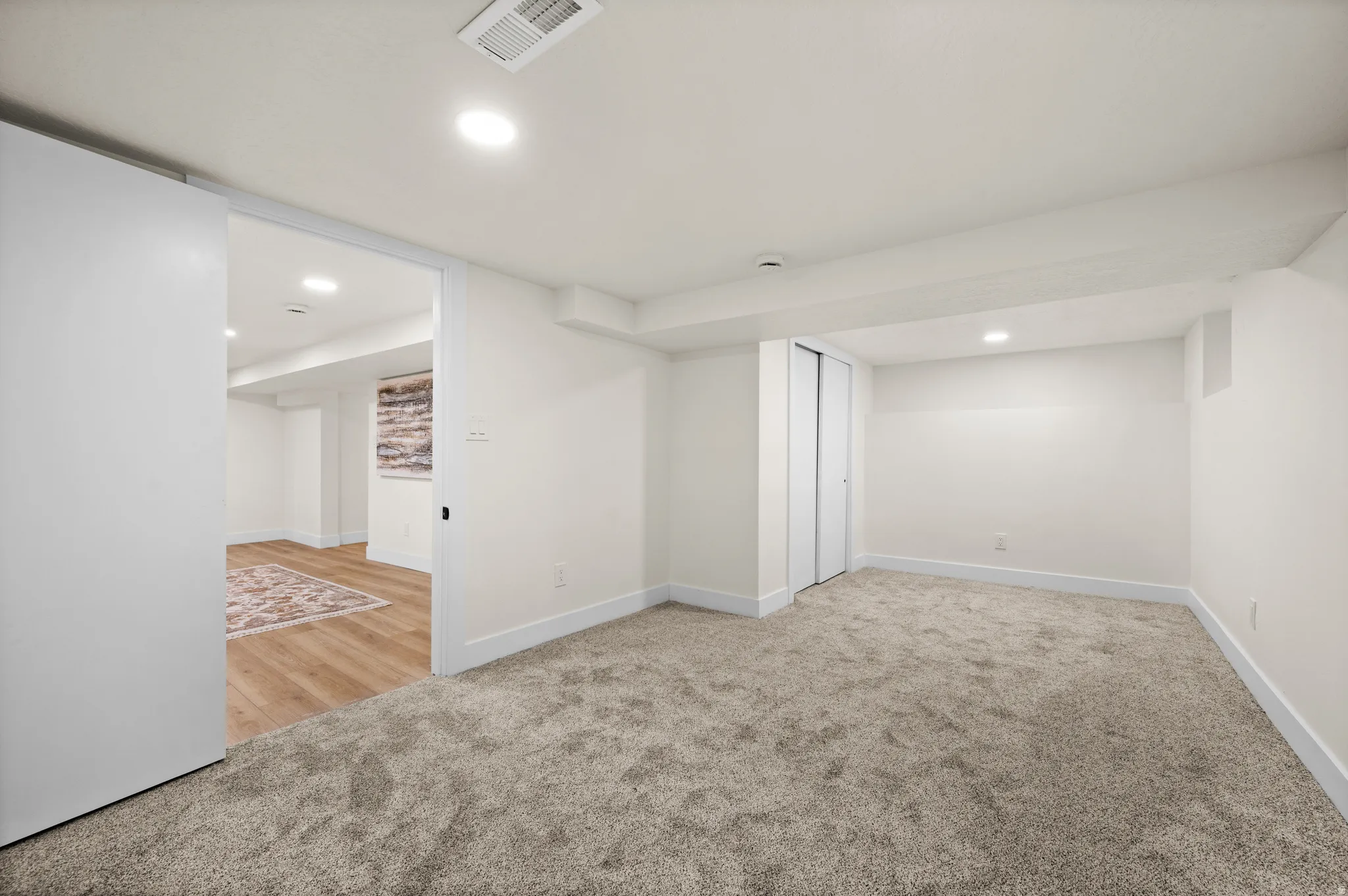 Carpeted room with recessed lighting and white walls, featuring a bypass closet and wide white baseboards