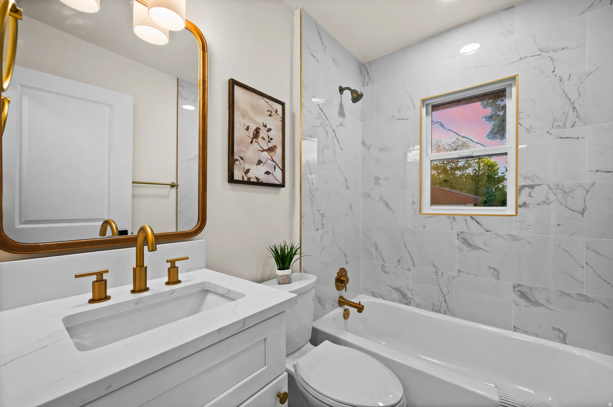 Bathroom featuring white marble-look wall tiling, a gold-framed mirror, and a vanity with a white countertop and integrated sink