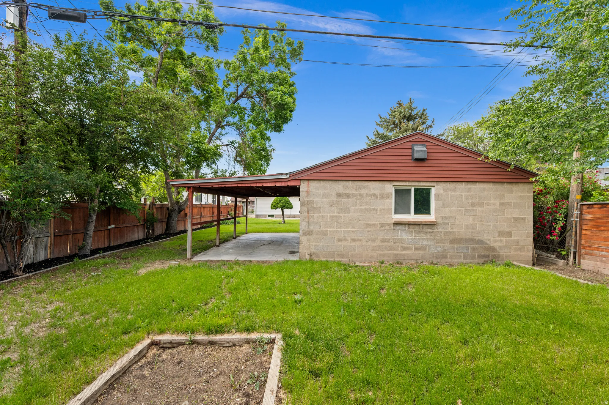 Expansive backyard featuring a concrete block structure with a red gable roof, an attached carport, and mature perimeter trees