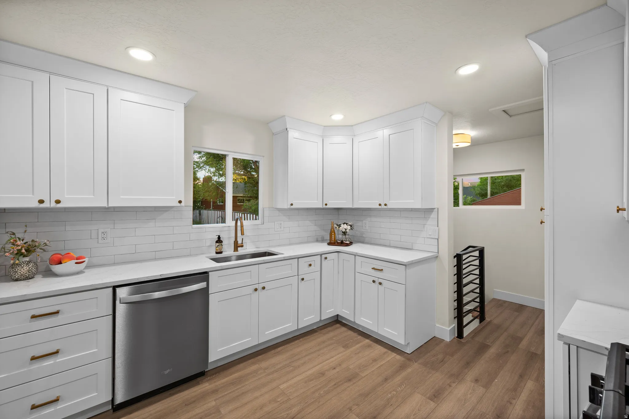 Bright kitchen featuring white shaker cabinetry, white subway tile backsplash, stainless steel dishwasher, and a bronze-finish faucet