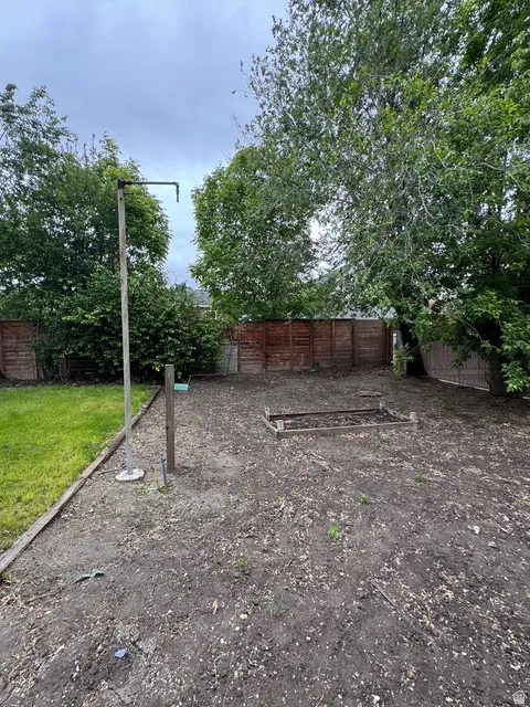 Spacious backyard area featuring a wood fence perimeter, a designated garden bed, and mature trees providing natural shading