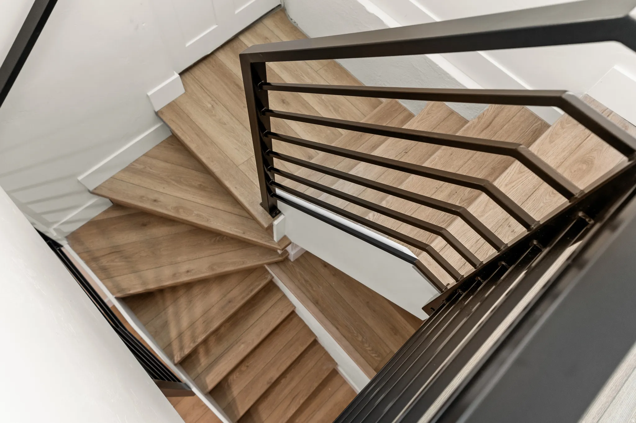 Staircase featuring light wood-finish treads, white risers, and black metal railings with horizontal spindles