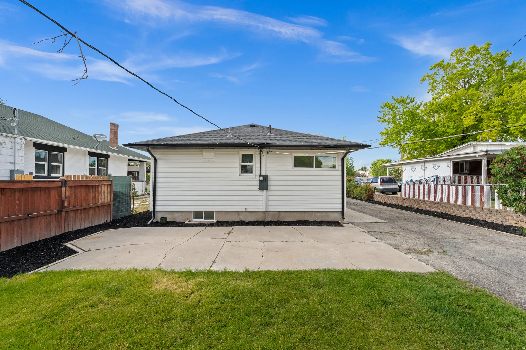 Rear exterior featuring white vinyl siding, a black shingle roof, a concrete patio, and a grass lawn