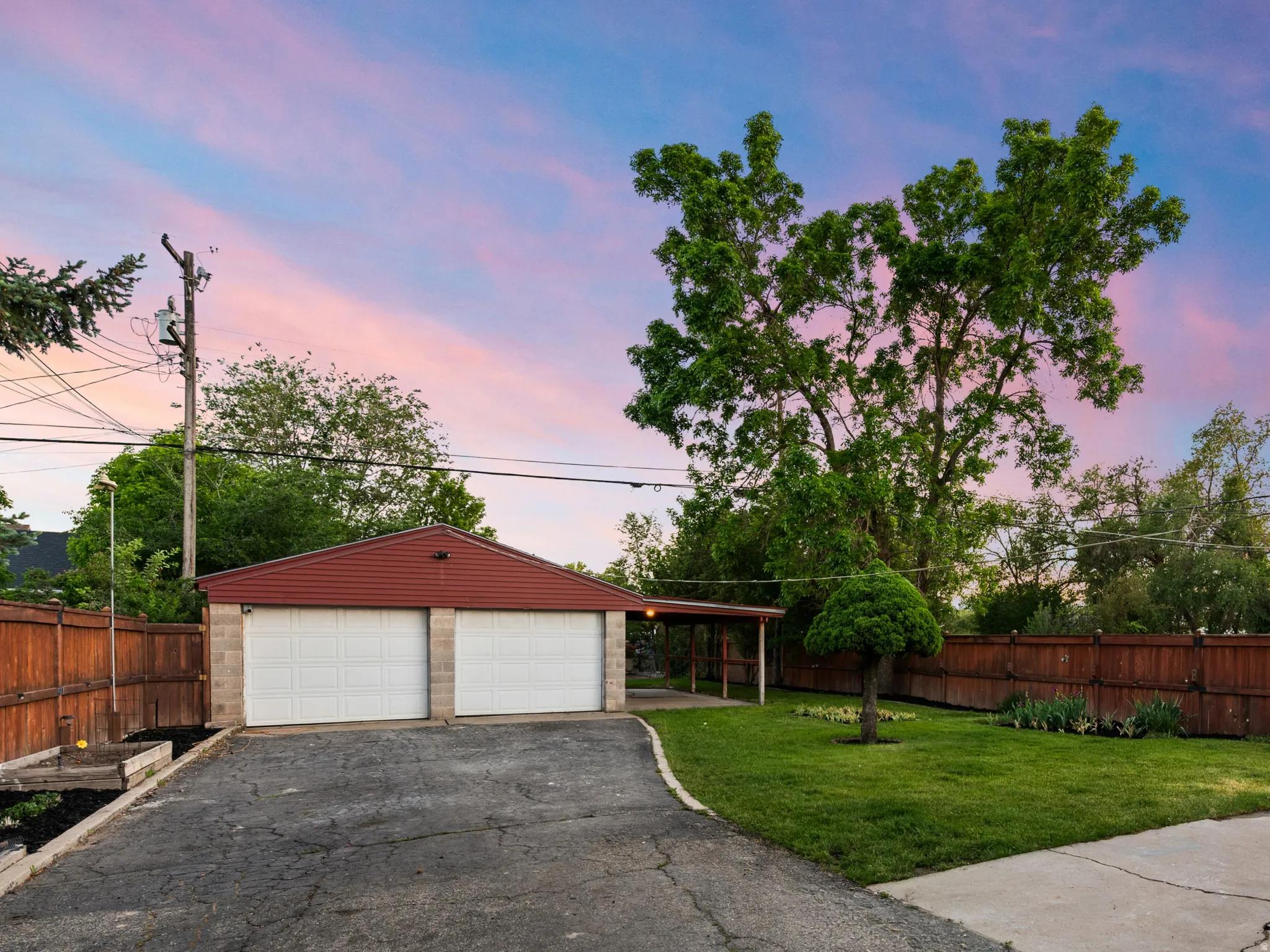 Detached two-car garage with white garage doors and a red roof, complemented by an extended covered carport
