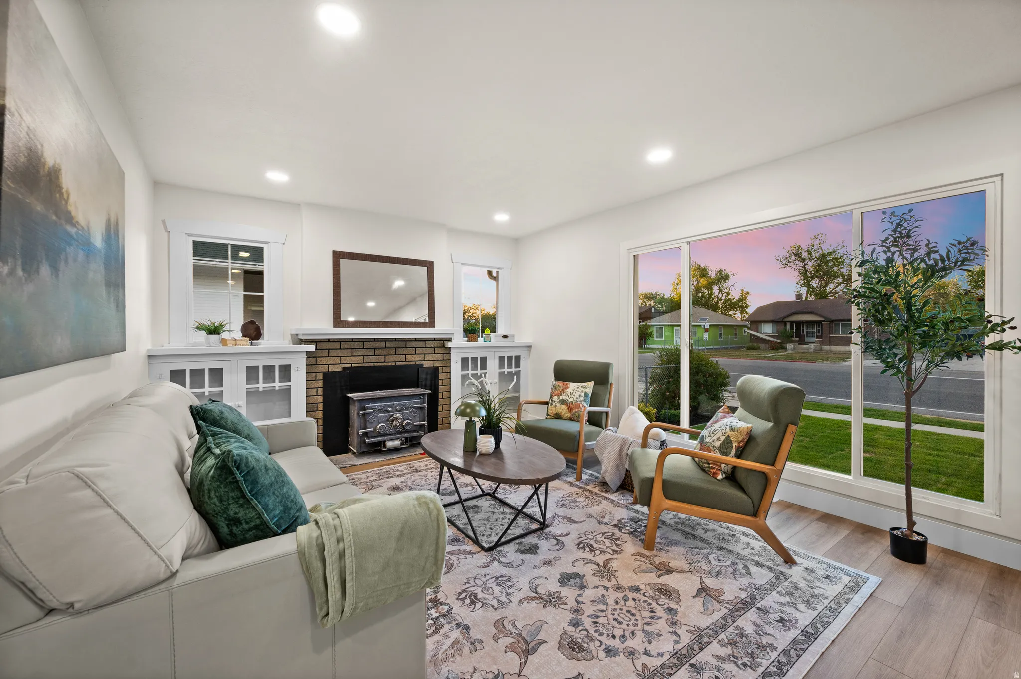 Living space featuring recessed lighting, large picture windows, wood-finish flooring, and a brick fireplace with a built-in wood-burning stove