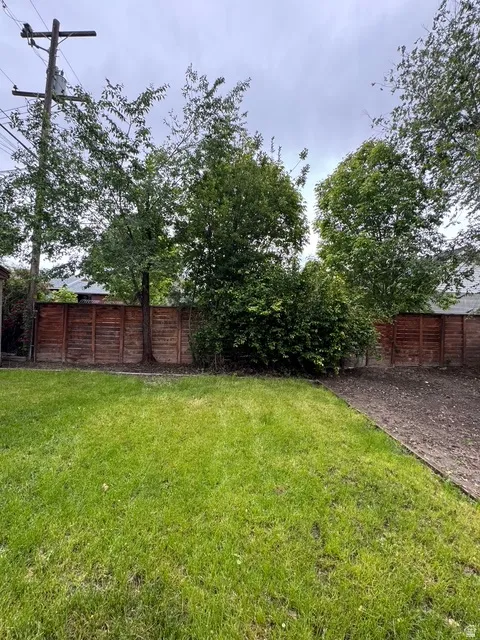 Expansive backyard featuring a large grassy area, a perimeter fence, and mature trees providing natural screening