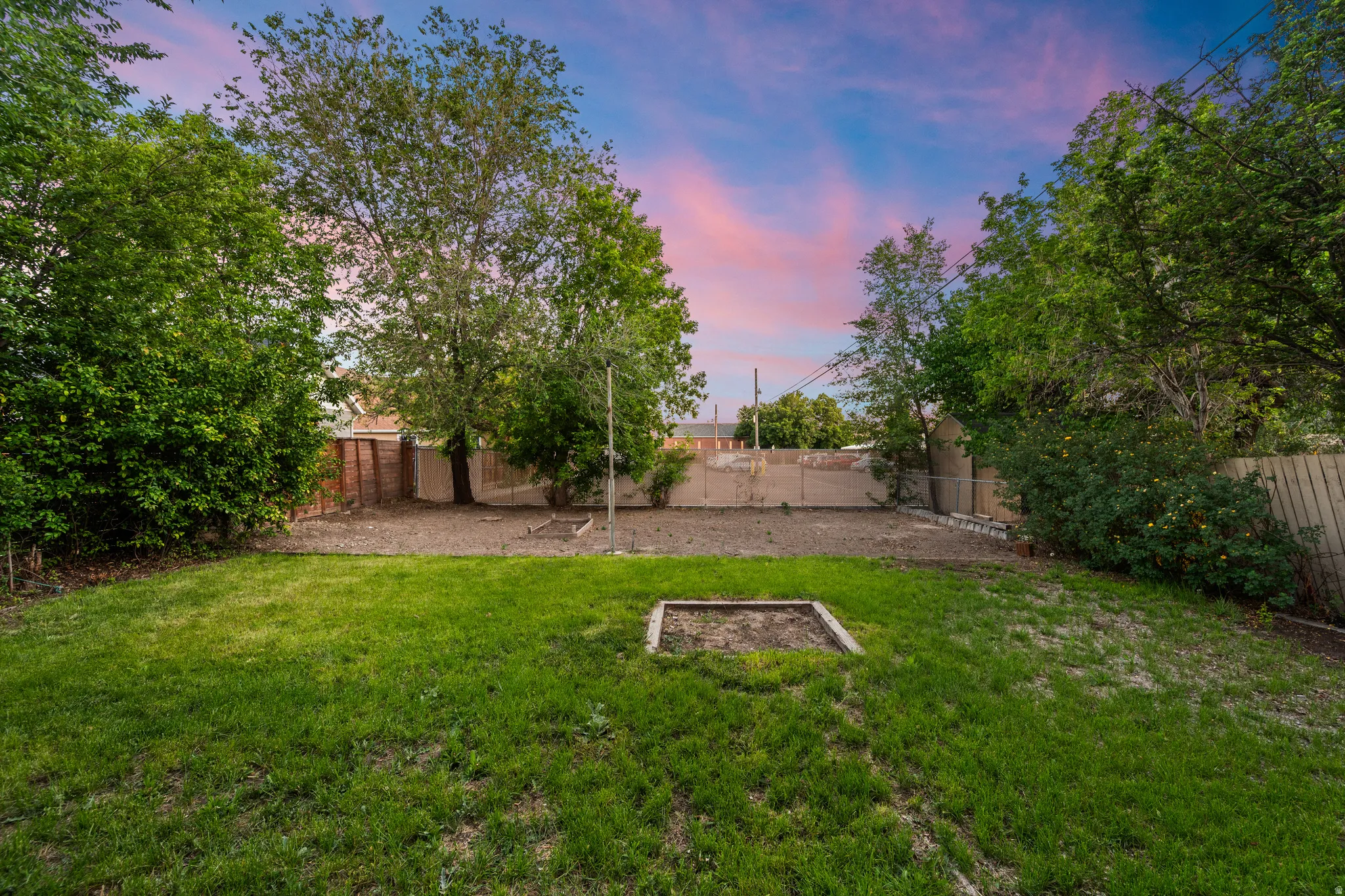 Spacious backyard featuring a manicured lawn, established trees, and a wooden perimeter fence