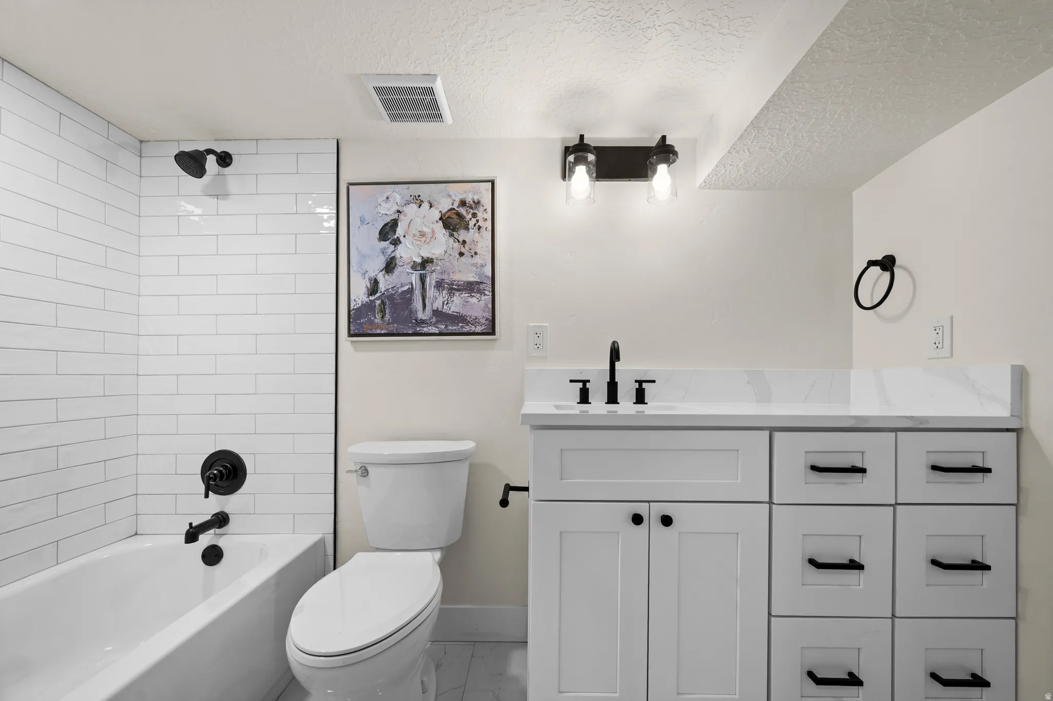 Full bathroom featuring a white subway tile tub surround, matte black fixtures, a white vanity with a stone-finish countertop, and a contemporary wall-mounted light fixture