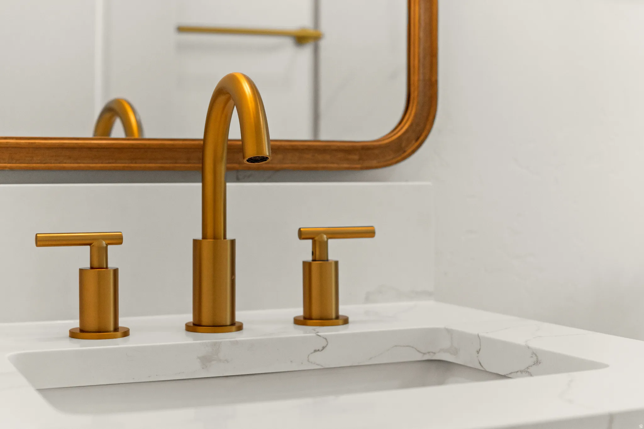 Integrated sink with white countertop featuring subtle veining, gold-tone faucet, and coordinating gold-tone mirror frame