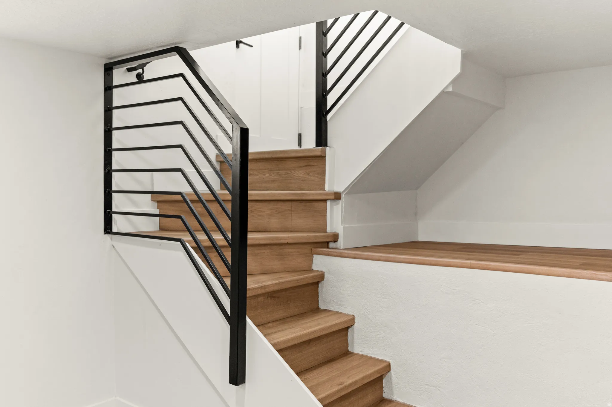 Contemporary staircase featuring wood-finish treads, black metal railings, and white painted walls