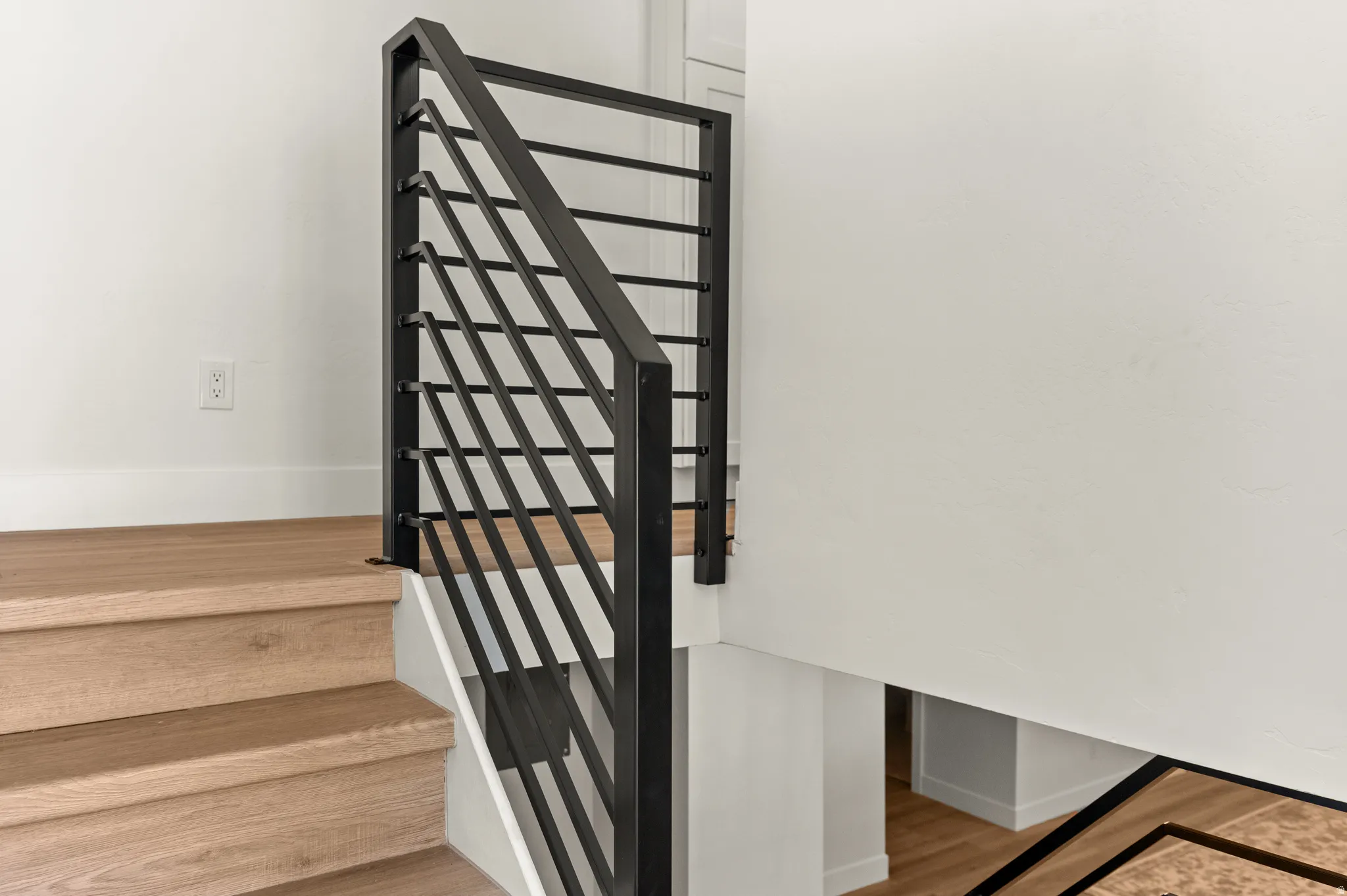 Staircase featuring light wood-finish treads and risers, white baseboards, and a contemporary black metal balustrade with horizontal railings