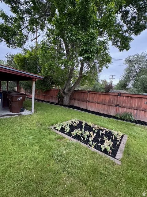Expansive backyard featuring a lush lawn, a mature shade tree, a raised garden bed with planted greenery, and a wood fence enclosing the perimeter