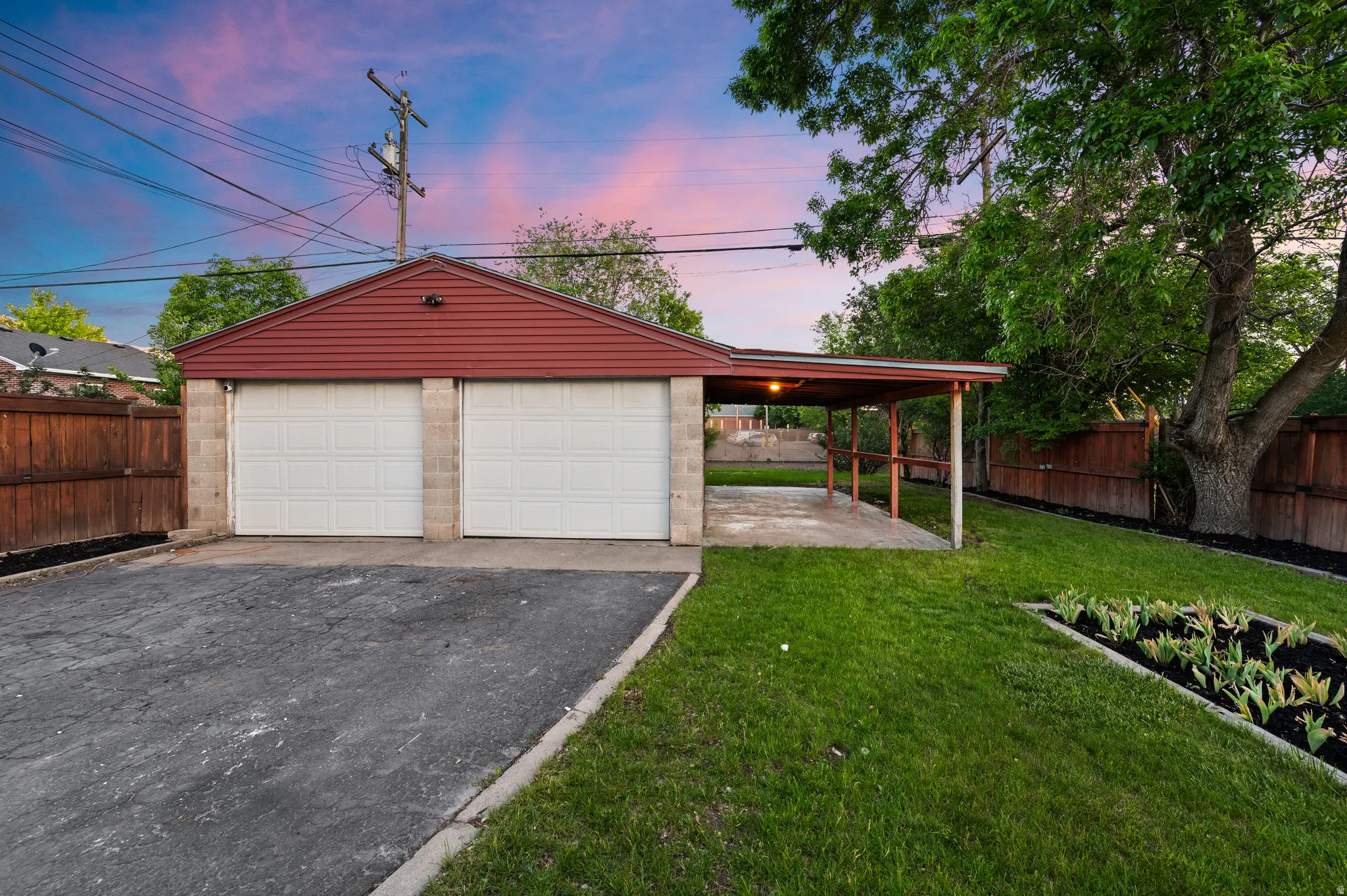 Detached two-car garage with red siding and a covered carport extension