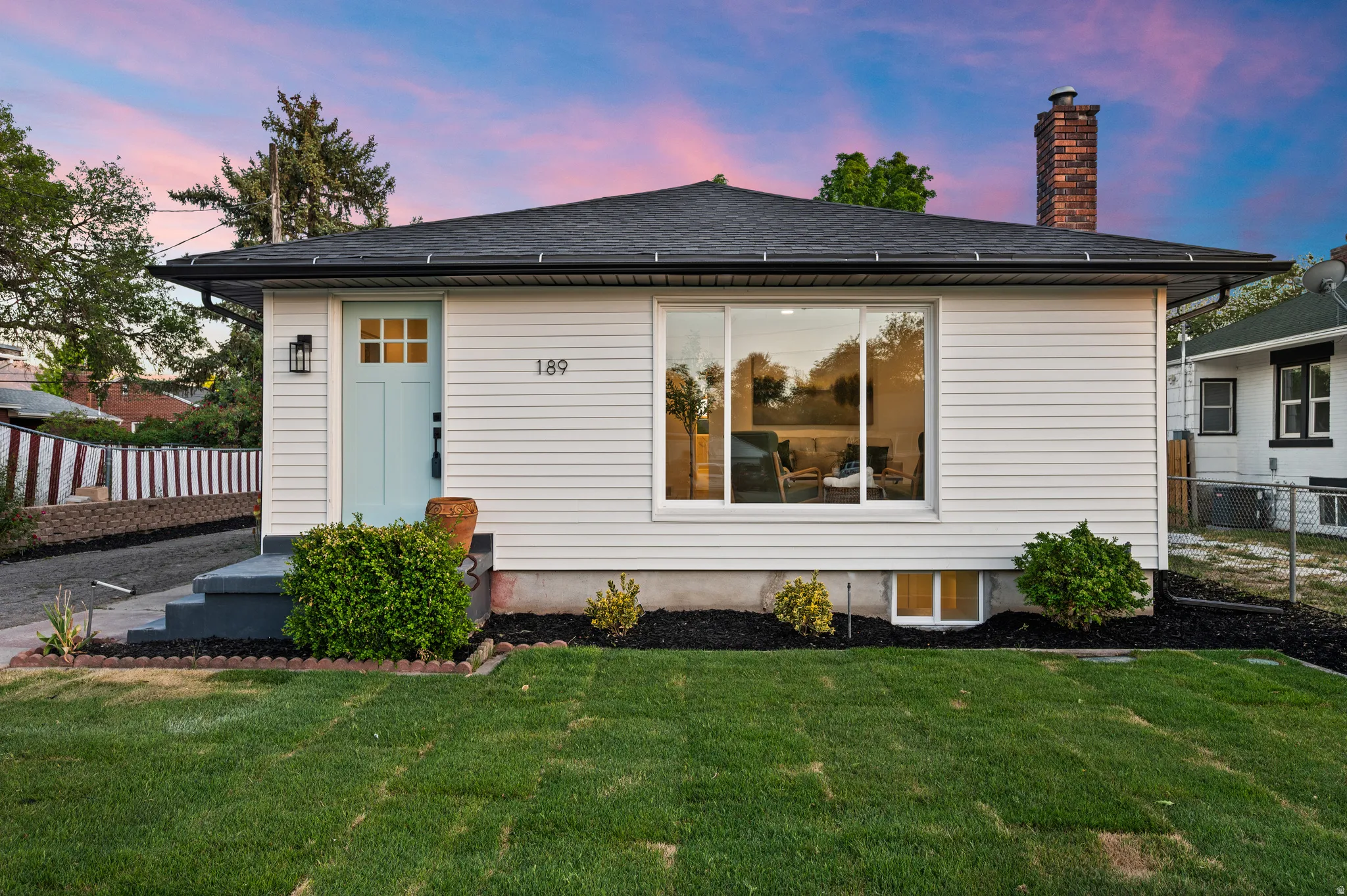 Single-story residence featuring white siding, a contrasting dark roof, and a prominent brick chimney